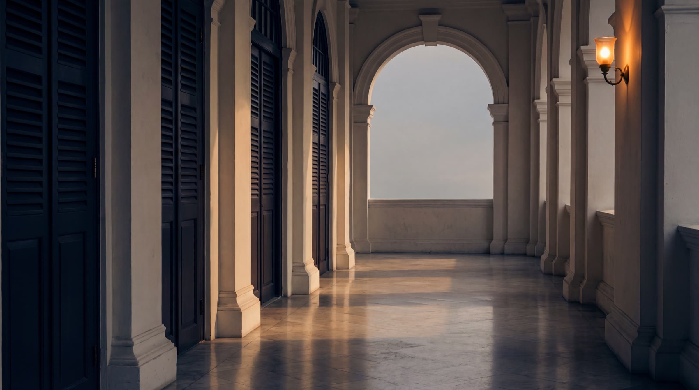 A colonial-era stone arcade at dawn, white-washed limestone columns receding off-axis under a brass-warm tropical morning light raking across the polished stone floor.
